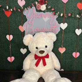 Large white teddy bear with a red bow in front of a heart-themed backdrop