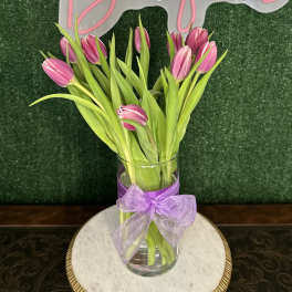 Pink tulips in a clear glass vase with a lavender ribbon