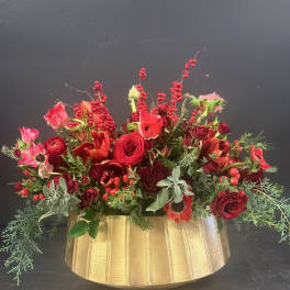 Red floral arrangement in a gold vase with berries and greenery
