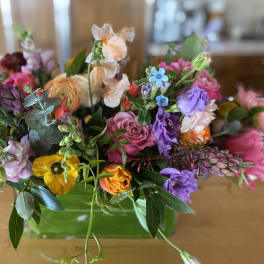 Mixed bouquet of purple, pink, peach, and yellow flowers in a glass vase