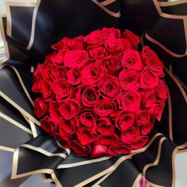 Round bouquet of red roses wrapped in black paper with gold trim