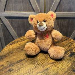 Brown teddy bear with red heart accents sitting on a wooden table