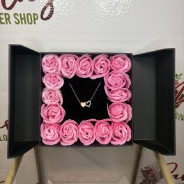 Pink roses arranged in a square gift box with a heart necklace in the center