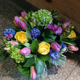 Compact bouquet of yellow roses, pink tulips, green hydrangeas and purple-blue hyacinths.