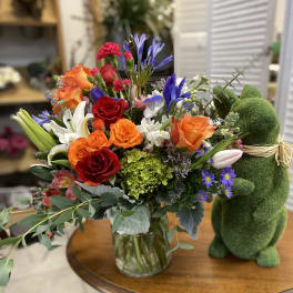 Mixed bouquet of roses, lilies, and purple flowers in a glass vase