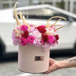 Pink and red roses arranged in a round hatbox with dried accents.