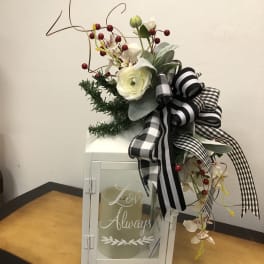 White floral arrangement with black plaid ribbon in a lantern vase