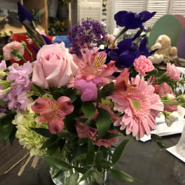 Mixed bouquet with pink roses, gerbera daisies, and purple blooms in a glass vase