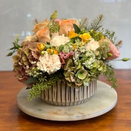 Mixed floral arrangement in a ribbed ceramic vase with peach, cream, and yellow blooms