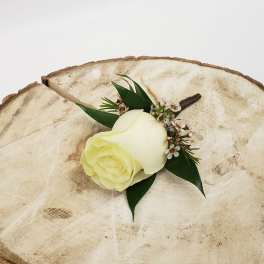 White rose boutonniere with small white blossoms on a wood slice