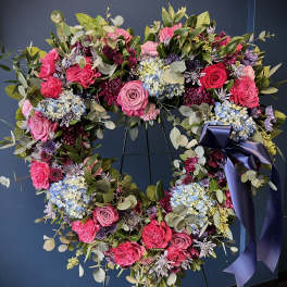 Heart-shaped floral wreath with pink, purple, and blue flowers on a dark stand