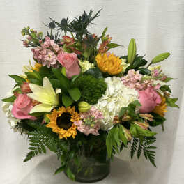 Mixed bouquet of pink roses, lilies, sunflowers, and white hydrangeas in a glass vase