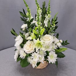 White floral arrangement in a wicker basket with lilies and roses
