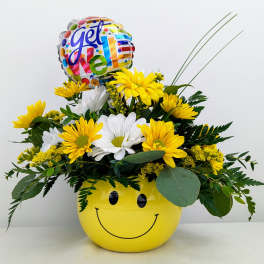 Yellow and white daisy arrangement in a smiley-face pot with a "Get Well" balloon