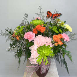 Colorful floral arrangement with roses, hydrangea, and a butterfly pick in a vase