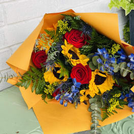 Bouquet of red roses, sunflowers, and blue flowers wrapped in orange paper