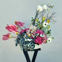 Pink and white floral arrangement in a white vase on a black stand