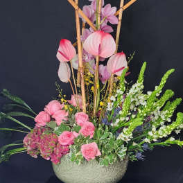 Pink orchids and roses arranged in a carved ceramic bowl