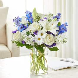 White lilies and roses with blue flowers in a clear glass vase