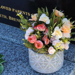 Mixed bouquet in a white textured vase beside a memorial plaque