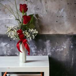 Red roses in a white vase with baby's breath and a red ribbon