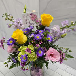 Mixed bouquet in a glass vase with yellow roses, pink blooms, and purple daisies