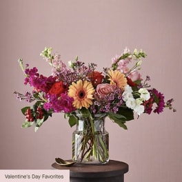 Mixed bouquet of pink, red, white, and peach flowers in a clear glass vase