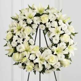 White floral wreath with lilies, roses, and daisies on a black stand