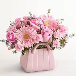 Pink roses and gerbera daisies in a pink handbag-shaped container