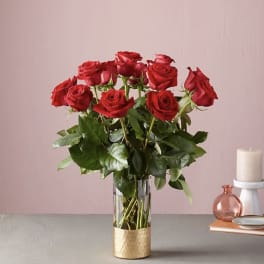 Red roses arranged in a clear glass vase with a gold base