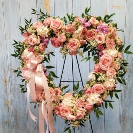 Heart-shaped floral wreath with pink roses and a satin ribbon on a stand