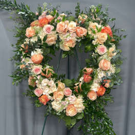 Heart-shaped floral wreath with peach and pink roses on a stand