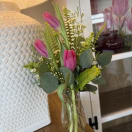Pink tulips in a clear glass vase with mixed greenery