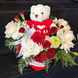 Teddy bear in a red sweater surrounded by red and white flowers
