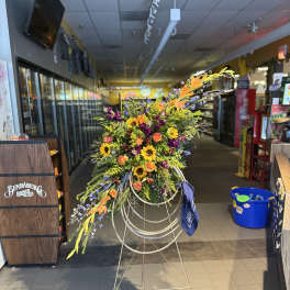 Large standing floral spray with sunflowers, orange roses, and purple blooms