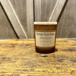 Brown jar candle with a beige label on a wooden surface