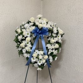 White floral funeral wreath on a stand with a blue ribbon