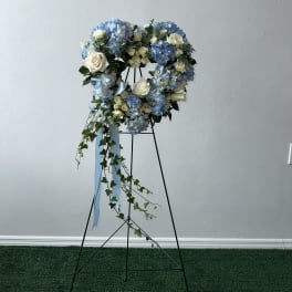 Heart-shaped floral wreath with blue hydrangeas and white roses on a stand
