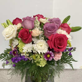 Mixed bouquet of roses, lilies, and daisies in a glass vase