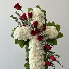 Standing cross of white flowers with red roses on an easel