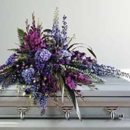 Purple and blue floral casket spray displayed on a silver casket