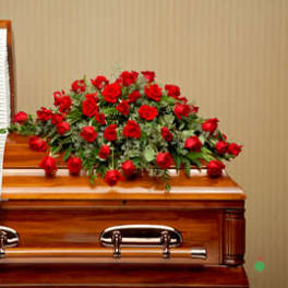 Red rose casket spray arranged on a polished wood casket with white interior lining.