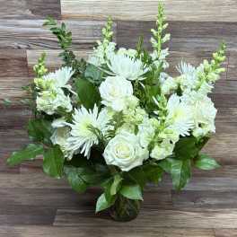 Arrangement of white roses, chrysanthemums, and snapdragons in a clear glass vase