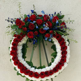 Standing floral wreath of red roses, white flowers, and blue accents on an easel