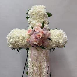 White floral cross with pink roses and ribbon on a stand