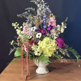 Tall mixed arrangement with pink, white, green, and purple flowers in a white pedestal vase.
