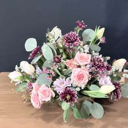 Pink roses and purple daisies arranged with white tulips in a low bouquet