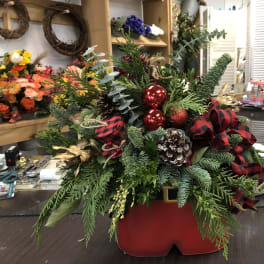 Holiday arrangement with evergreen branches, red ornaments, and plaid ribbon in a red container