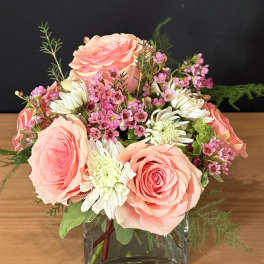 Pink roses and white daisies arranged in a square glass vase.