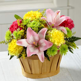 Basket arrangement with pink lilies, yellow and green carnations, and red blooms